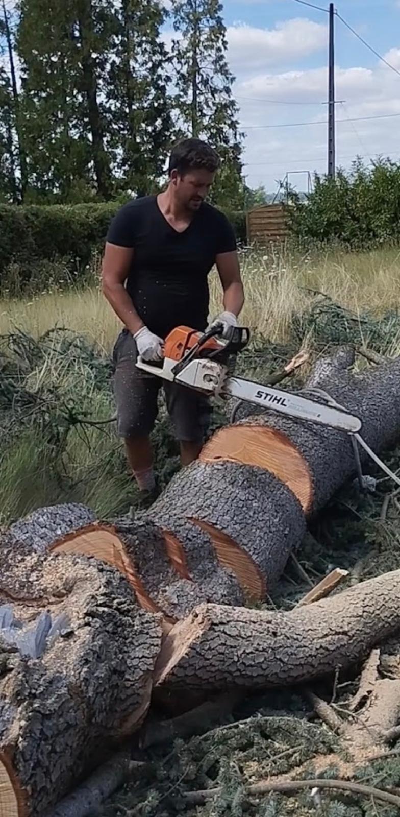 Élagueur avec une tronçonneuse devant un tronc au sol dans un jardin